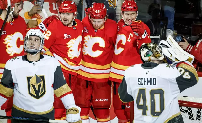 Vegas Golden Knights' Zach Whitecloud, front left, and goalie Akira Schmid, right, look away as Calgary Flames' Mikael Backlund, back right, celebrates after scoring during second-period NHL hockey game action in Calgary, Saturday, Dec. 20, 2025. (Jeff McIntosh/The Canadian Press via AP)