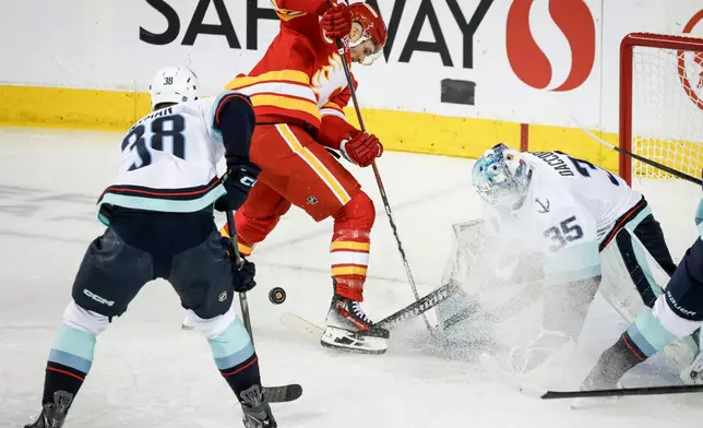 Seattle Kraken goalie Joey Daccord (35) hits the puck away from Calgary Flames' Jonathan Huberdeau, center top, during second-period NHL hockey game action in Calgary, Alberta, Thursday, Dec. 18, 2025. (Jeff McIntosh/The Canadian Press via AP)