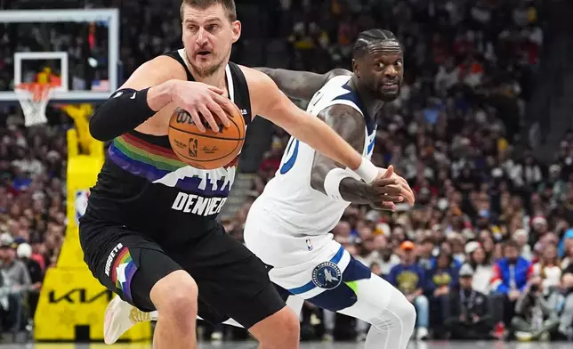 Denver Nuggets center Nikola Jokić, front, dribbles past Minnesota Timberwolves center Julius Randle in the first half of an NBA basketball game, Thursday, Dec. 25, 2025, in Denver. (AP Photo/David Zalubowski)