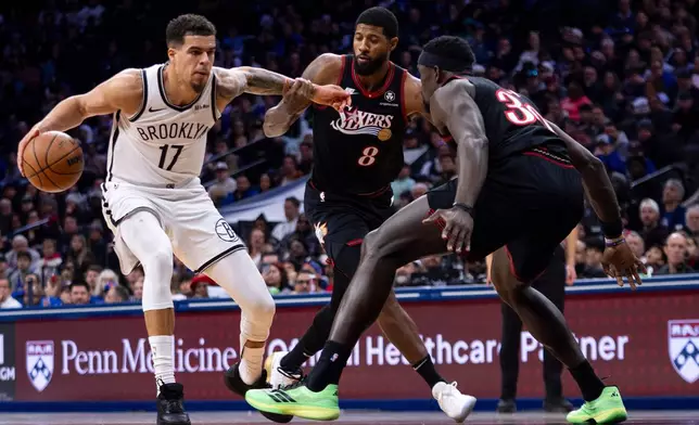 Brooklyn Nets' Michael Porter Jr., left, makes his move against Philadelphia 76ers' Paul George, center, and Adem Bona, right, during the first half of an NBA basketball game, Tuesday, Dec. 23, 2025, in Philadelphia. (AP Photo/Chris Szagola)
