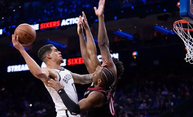 Brooklyn Nets' Michael Porter Jr., left, shots the ball against Philadelphia 76ers' Tyrese Maxey, center and Joel Embiid, right, during the first half of an NBA basketball game, Tuesday, Dec. 23, 2025, in Philadelphia. (AP Photo/Chris Szagola)