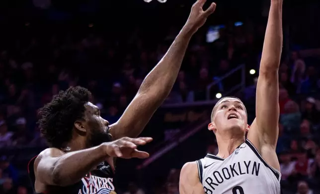 Brooklyn Nets' Egor Demin, right, shoots the ball against Philadelphia 76ers' Joel Embiid, left, during the first half of an NBA basketball game, Tuesday, Dec. 23, 2025, in Philadelphia. (AP Photo/Chris Szagola)