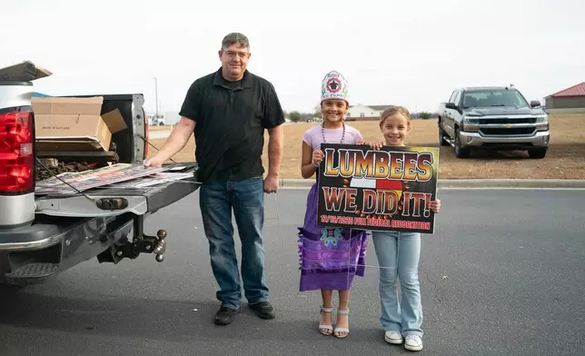 Children pose for a photo with a man selling signs after passage of the National Defense Authorization Act by the U.S. Senate, during a watch party hosted by the Lumbee Tribe of North Carolina, Wednesday, Dec. 17, 2025, in Pembroke, N.C. (AP Photo/Allison Joyce)