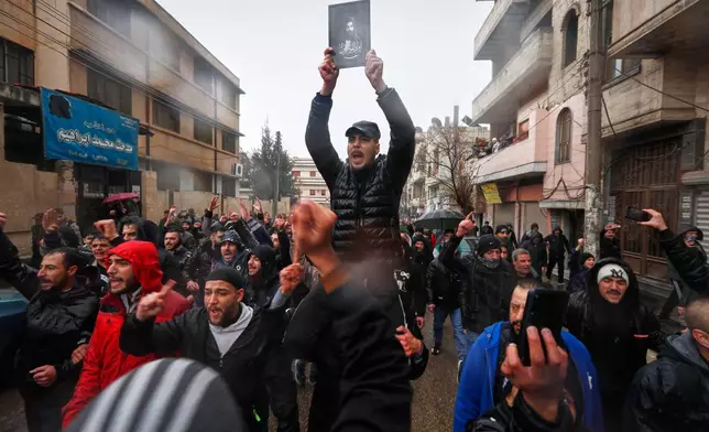A man holds an imaginary depiction of Ali ibn Abi Talib, the cousin and son-in-law of the Prophet Muhammad who is revered by Syria's Alawite community, during the funeral of victims of an attack a day earlier at the Imam Ali bin Abi Talib Mosque in the predominantly Alawite Wadi al-Dhahab neighborhood of Homs, Syria, Saturday, Dec. 27, 2025. (AP Photo/Omar Sanadiki)