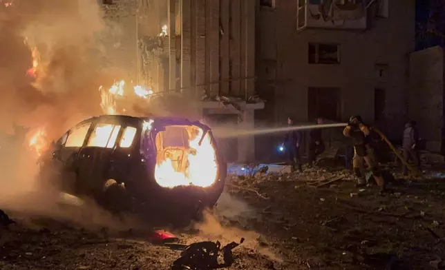 In this photo provided by the Ukrainian Emergency Services on Monday, Dec. 8, 2025, a rescue worker puts out a fire of a car in front of a residential building damaged by a Russian strike in Sumy region, Ukraine. (Ukrainian Emergency Service via AP)