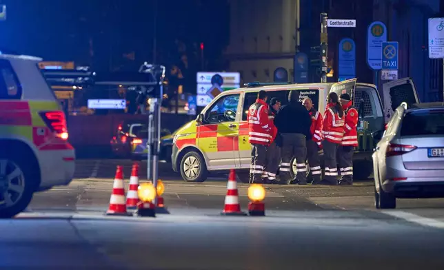 Emergency services from the German Red Cross (DRK) stand next to an emergency vehicle, at the site where a car is said to have driven into a bus stop and several people were injured, according to the police, in Giessen, Germany, Monday Dec. 22, 2025. (Sascha Ditscher/dpa via AP)