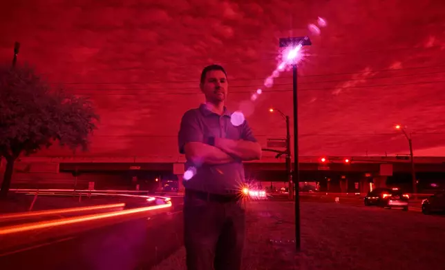 Alek Schott, who filed a lawsuit alleging violations of his constitutional rights when Texas sheriff's deputies stopped and searched his vehicle at the request of Border Patrol agents, is photographed, as an infrared beam of light from a Flock Safety automatic license plate reader records passing vehicles driving near his neighborhood, Oct. 16, 2025, in Houston. (AP Photo/David Goldman)
