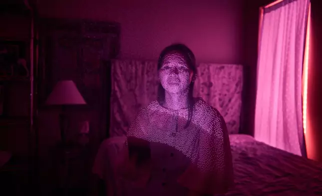 Dong e Li, a member of a Chinese church living in exile after fleeing from China, is illuminated by cellphone infrared facial recognition beams as she sits for a photo in her home, Oct. 13, 2025, in Midland, Texas. (AP Photo/David Goldman)