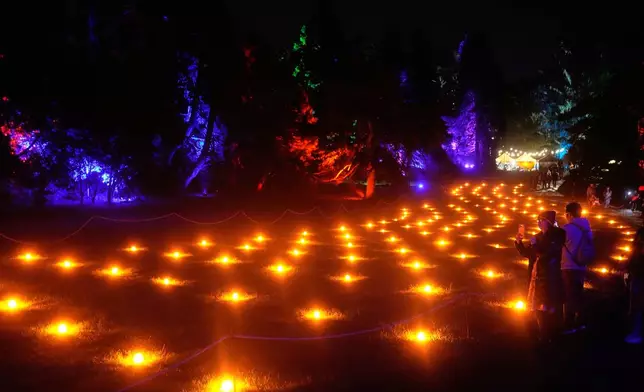 People look toward lights illuminating the San Francisco Botanical Garden's Fire Garden exhibit for Lightscape at Golden Gate Park in San Francisco, Wednesday, Dec. 17, 2025. (AP Photo/Jeff Chiu)