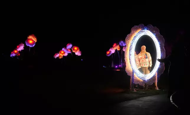 People have their photos taken in front of the San Francisco Botanical Garden's Peonies exhibit for Lightscape at Golden Gate Park in San Francisco, Wednesday, Dec. 17, 2025. (AP Photo/Jeff Chiu)