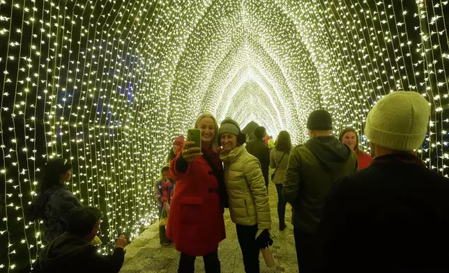 People take photos while walking through the San Francisco Botanical Garden's Winter Cathedral exhibit for Lightscape at Golden Gate Park in San Francisco, Wednesday, Dec. 17, 2025. (AP Photo/Jeff Chiu)
