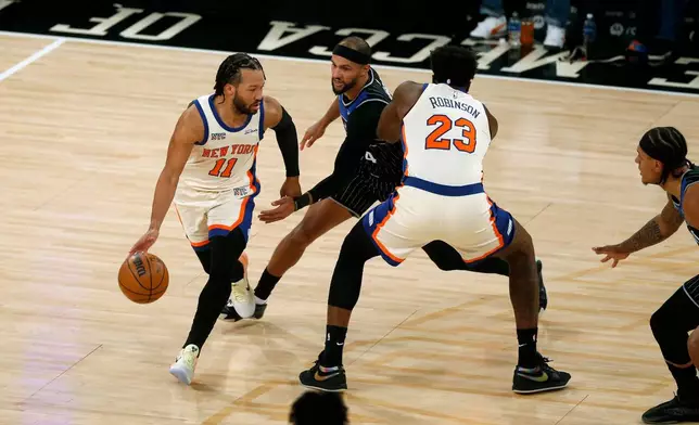 New York Knicks guard Jalen Brunson, left, dribbles around Orlando Magic guard Jalen Suggs, middle, and Knicks center Mitchell Robinson during the first half of an NBA basketball game Sunday, Dec. 7, 2025, in New York. (AP Photo/John Munson)