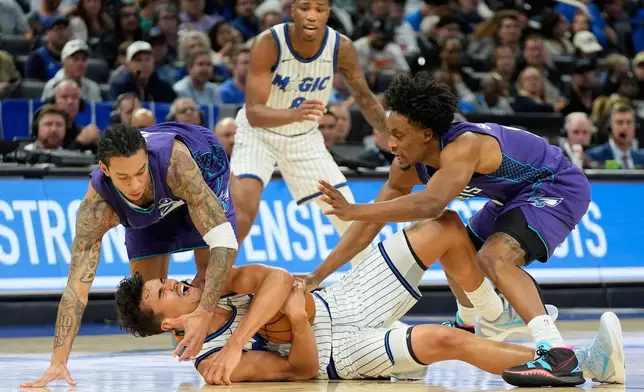 Orlando Magic forward Tristan da Silva, center, tries to maintain possession of a loose ball against Charlotte Hornets guard Tre Mann, left, and guard Sion James, right, during the second half of an NBA basketball game, Friday, Dec. 26, 2025, in Orlando, Fla. (AP Photo/John Raoux)