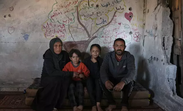 Amani and Mohammed Halawa pose for a picture with their children, Aya, 13, and Bashir, 10, inside their partially collapsed home, with a tree and messages of longing and hope painted on the wall behind them, Jabaliya, Gaza City, Tuesday, Nov. 25, 2025.(AP Photo/Jehad Alshrafi)