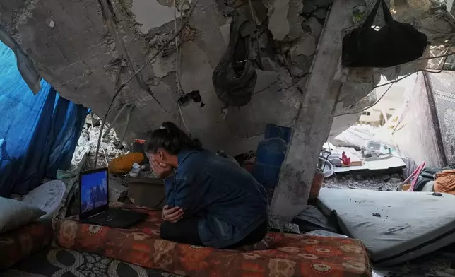 Bisan Taroush watches a movie on a laptop beneath the partially collapsed roof of her home, carrying on with daily life amid the ruins, in Jabaliya, Gaza City, Tuesday, Nov. 11, 2025. (AP Photo/Jehad Alshrafi)
