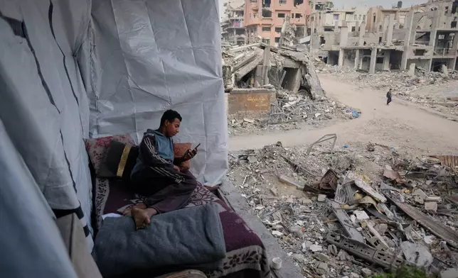 Omar Qutay sits on a bed placed on the balcony of his partially destroyed home in the Al-Karama neighborhood of Gaza City, Wednesday, Nov. 24, 2025. (AP Photo/Jehad Alshrafi)