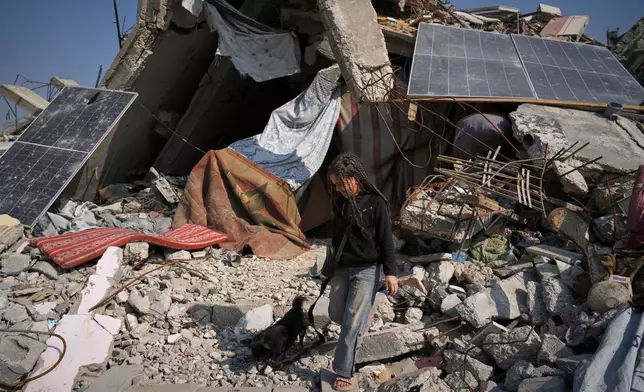 Rita Abu Shaqfa plays with her dog in front of their collapsed home, where the family struggles to live using damaged solar panels, in Jabaliya, Gaza City, Friday, Nov. 21, 2025. (AP Photo/Jehad Alshrafi)