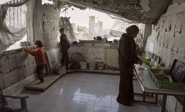 Amani Halawa prepares food beneath the half-collapsed roof of her home, with her children Aya, 13, and Bashir, 10, by her side as they try to carry on daily life amid the rubble, in Jabaliya, Gaza City, Tuesday, Nov. 25, 2025. (AP Photo/Jehad Alshrafi)