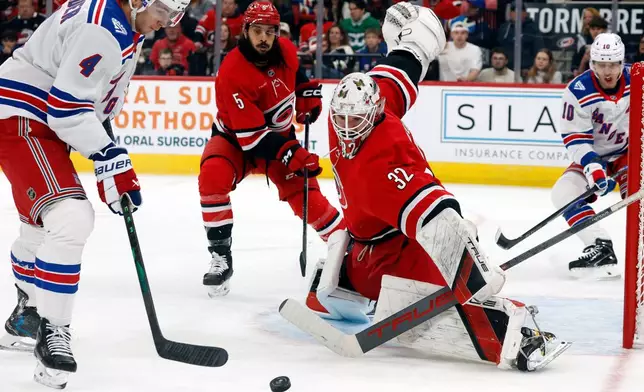 New York Rangers' Braden Schneider (4) tries to gather in the puck in front of Carolina Hurricanes goaltender Brandon Bussi (32) with Jalen Chatfield (5) nearby during the first period of an NHL hockey game in Raleigh, N.C., Monday, Dec. 29, 2025. (AP Photo/Karl DeBlaker)