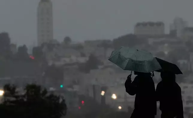 People carry umbrellas while walking on a path at Alamo Square Park, in San Francisco, Tuesday, Dec. 23, 2025. (AP Photo/Jeff Chiu)