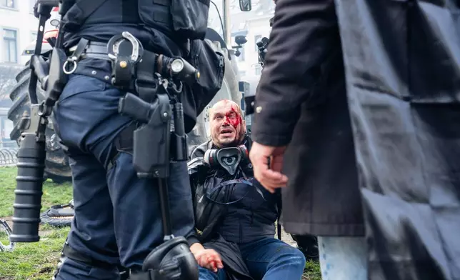 A protestor sits on a curb injured during a demonstration of European farmers near the European Parliament in Brussels, Thursday, Dec. 18, 2025. (AP Photo/Marius Burgelman)