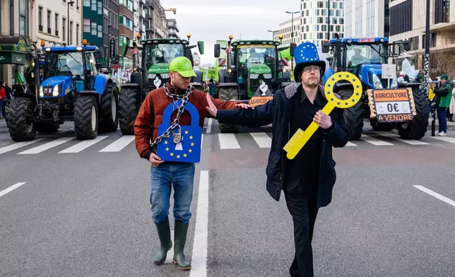 Two men walk in front of tractors during a demonstration of European farmers outside the EU Summit meeting in Brussels, Thursday, Dec. 18, 2025. (AP Photo/Marius Burgelman)