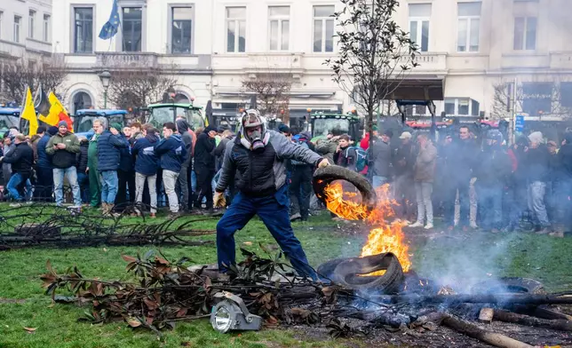 A protestor picks up a burning tire during a demonstration of European farmers outside the EU Summit meeting in Brussels, Thursday, Dec. 18, 2025. (AP Photo/Marius Burgelman)