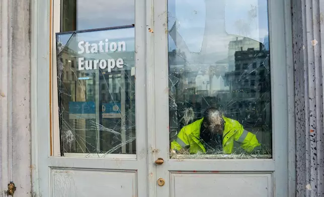 A man looks through a broken window of a visitors center that was damaged after a demonstration of European farmers at the European Parliament in Brussels, Thursday, Dec. 18, 2025. (AP Photo/Marius Burgelman)
