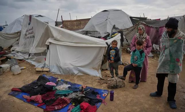Raafat Alwan, 32, right, and his family stand outside their tent as their clothes lie over a tarp to dry in a makeshift camp for displaced Palestinians set up on the beach during a cold morning in Gaza City, Tuesday, Dec. 16, 2025. (AP Photo/Abdel Kareem Hana)