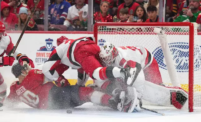 Florida Panthers left wing A.J. Greer and Carolina Hurricanes defenseman Sean Walker collide into goaltender Brandon Bussi during the second period of an NHL hockey game, Friday, Dec. 19, 2025, in Sunrise, Fla. (AP Photo/Jim Rassol)