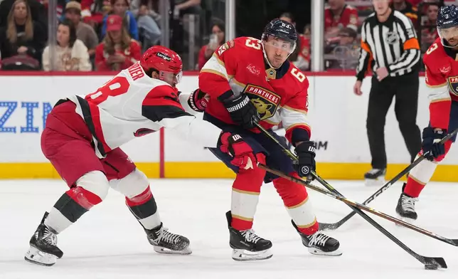 Florida Panthers left wing Brad Marchand (63) looks to pass the puck as Carolina Hurricanes left wing William Carrier, left, defends during the first period of an NHL hockey game Friday, Dec. 19, 2025, in Sunrise, Fla. (AP Photo/Jim Rassol)