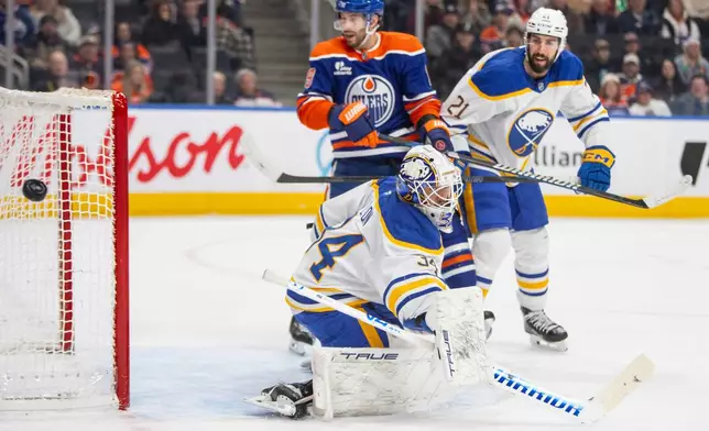 Buffalo Sabres goalie Alex Lyon (34) bats the puck away as Edmonton Oilers Adam Henrique (19) and Conor Timmins (21) look on during second period NHL action in Edmonton, Tuesday, Dec. 9, 2025. (Amber Bracken/The Canadian Press via AP)