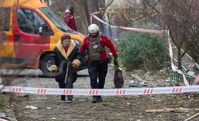 A paramedic evacuates an elderly resident after a Russian drone hit an apartment building during an aerial attack in Kyiv, Ukraine, Tuesday, Dec. 23, 2025. (AP Photo/Efrem Lukatsky)