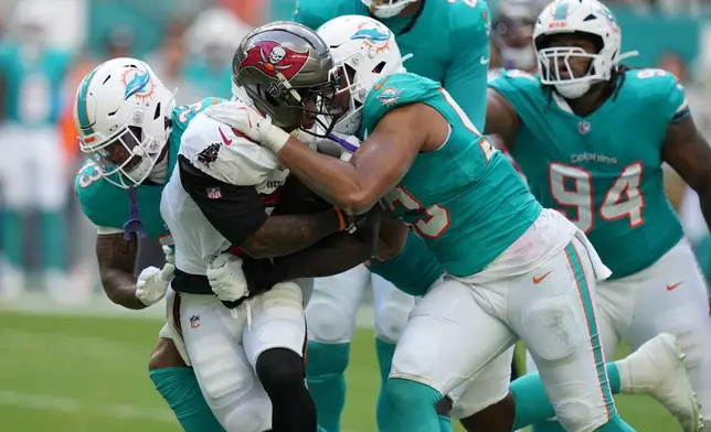 Miami Dolphins defensive tackle Zeek Biggers, front right, and cornerback Jason Marshall Jr. (33) tackle Tampa Bay Buccaneers running back Bucky Irving, second from left, during the first half of an NFL football game Sunday, Dec. 28, 2025, in Miami Gardens, Fla. (AP Photo/Lynne Sladky)