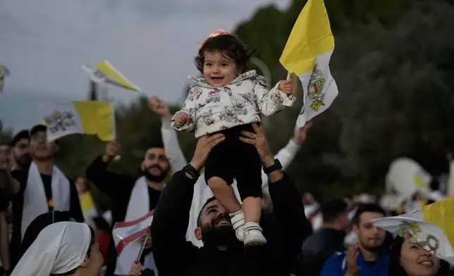 A man lifts a child holding a Vatican flag ahead of a visit by Pope Leo XIV to Bkerki, the seat of the Maronite Church, in Lebanon, Monday, Dec. 1, 2025. (AP Photo/Bilal Hussein)