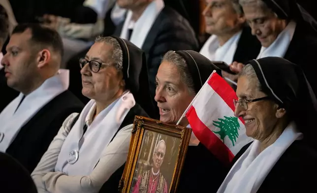 A nun holds a Lebanese flag and a portrait of Pope Leo XIV as he gathers with worshippers at the Catholic basilica of Harissa, Lebanon, Monday, Dec. 1, 2025. (AP Photo/Hussein Malla)