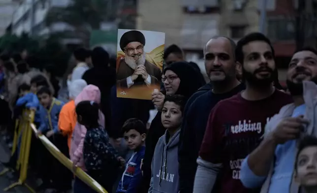 A woman holds a pictures of Hezbollah's former leader Hassan Nasrallah as people wait to welcome Pope Leo XIV upon his arrival to Beirut, Lebanon, Sunday, Nov. 30, 2025. (AP Photo/Bilal Hussein)