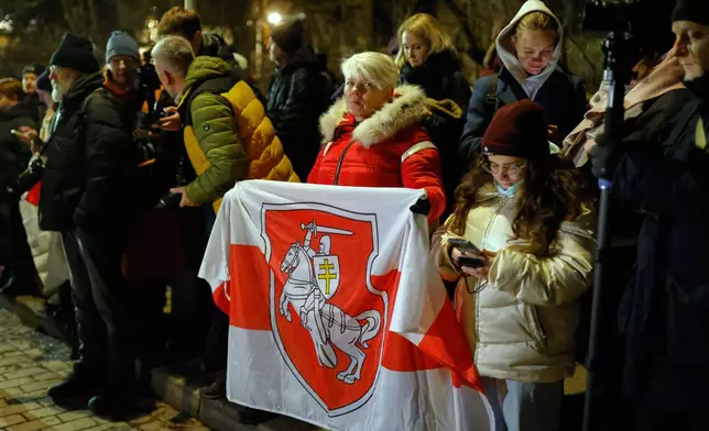 A woman holds an Old Belarusian flag as she stands waiting released Belarusian prisoners at the U.S. Embassy in Vilnius, Lithuania, on Saturday, Dec. 13, 2025. (AP Photo/Mindaugas Kulbis)