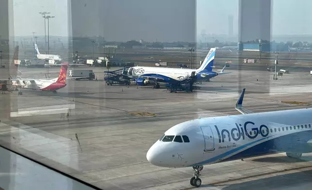 Two Indigo Airlines planes are seen through a glass window at the Indira Gandhi International Airport in New Delhi as several flights operated by the carrier were either cancelled or delayed, India, Thursday, Dec. 4, 2025. (AP Photo/Manish Swarup)
