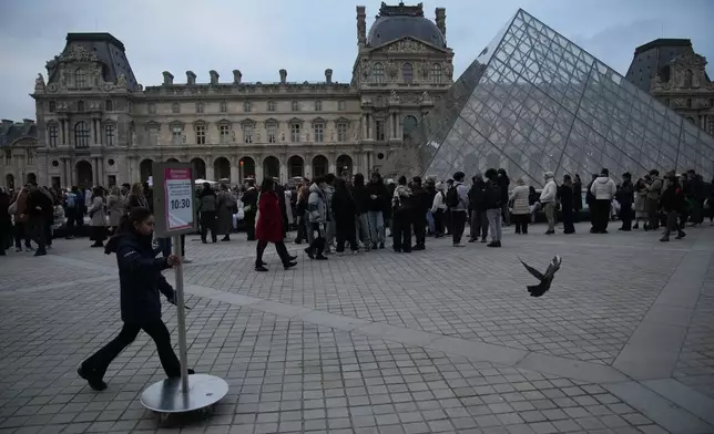 People wait at the entrance of the Louvre museum as employees were set to vote on whether to extend a strike that shut the world's most visited museum, as unions protest chronic understaffing, building deterioration and recent management decisions Wednesday, Dec. 17, 2025 in Paris. (AP Photo/Christophe Ena)