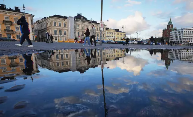 People walking along the square are reflected in a puddle in Helsinki, Finland, Friday, Nov. 14, 2025. (AP Photo/Sergei Grits)