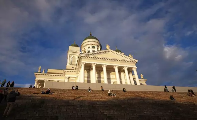 People enjoy the sunny weather with the Helsinki Cathedral of the background in Helsinki, Finland, Friday, Nov. 14, 2025. (AP Photo/Sergei Grits)