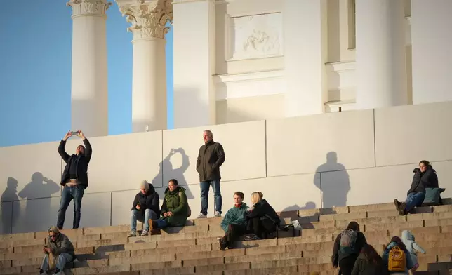 People enjoy the sunny weather with the Helsinki Cathedral of the background in Helsinki, Finland, Friday, Nov. 14, 2025. (AP Photo/Sergei Grits)