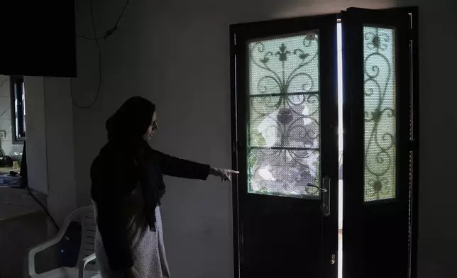 Wafaa Rabie, 30, shows the door of her house that was damaged during an Israeli settlers attack in the town of As Samu', near the West Bank city of Hebron, Tuesday, Dec. 23, 2025. (AP Photo/Mahmoud Illean)