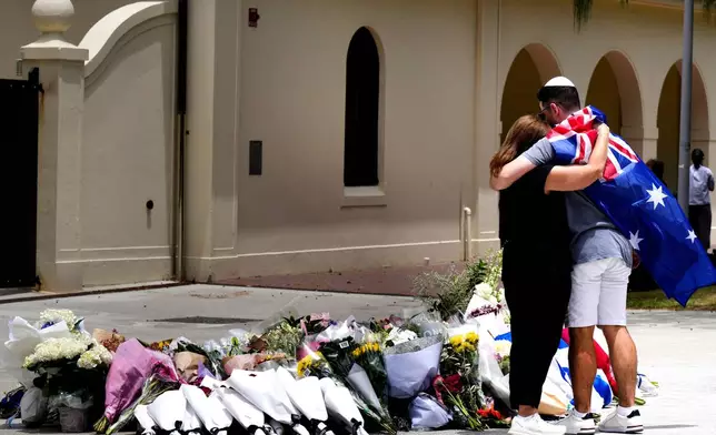 A couple lay flowers at a tribute to shooting victims outside the Bondi Pavilion at Sydney's Bondi Beach, Monday, Dec. 15, 2025, a day after a shooting. (AP Photo/Mark Baker)