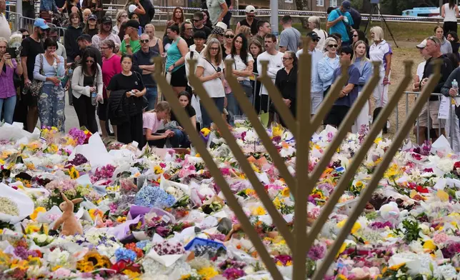A Hanukkah menorah stands by a floral tribute as people gather to pay their respects near the Bondi Pavilion at Bondi Beach on Tuesday, Dec. 16, 2025, following Sunday's shooting in Sydney, Australia. (AP Photo/Mark Baker)