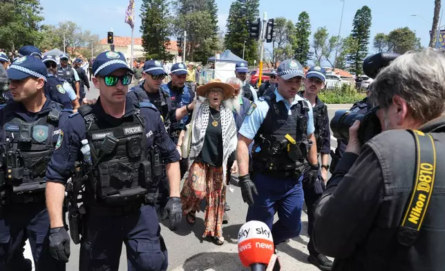A woman is escorted from a flower memorial outside the Bondi Pavilion at Sydney's Bondi Beach, Monday, Dec. 15, 2025, a day after a shooting. (AP Photo/Mark Baker)