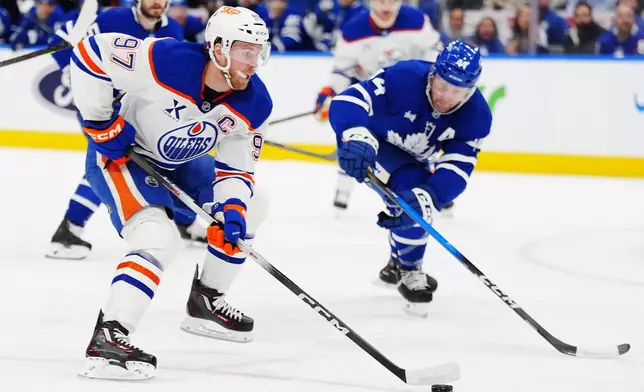 Edmonton Oilers' Connor McDavid (97) skates past Toronto Maple Leafs' Morgan Rielly, right, during the first period of an NHL hockey game in Toronto, Saturday, Dec. 13, 2025. (Frank Gunn/The Canadian Press via AP)