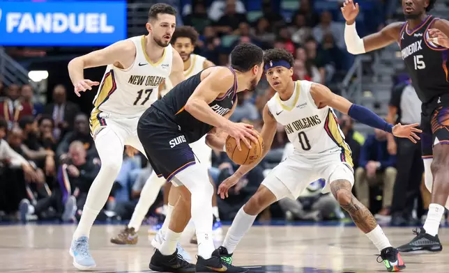 Phoenix Suns guard Devin Booker, center, tries to make a move against New Orleans Pelicans forward Karlo Matkovic (17) and guard Jeremiah Fears (0) in the first half of an NBA basketball game Friday, Dec. 26, 2025, in New Orleans. (AP Photo/Peter Forest)
