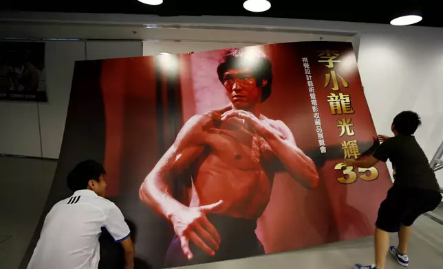 FILE - Workers carry a poster of Bruce Lee as part of an exhibition marking the 35th anniversary of his death, on July 18, 2008, in Hong Kong. (AP Photo/Vincent Yu, File)